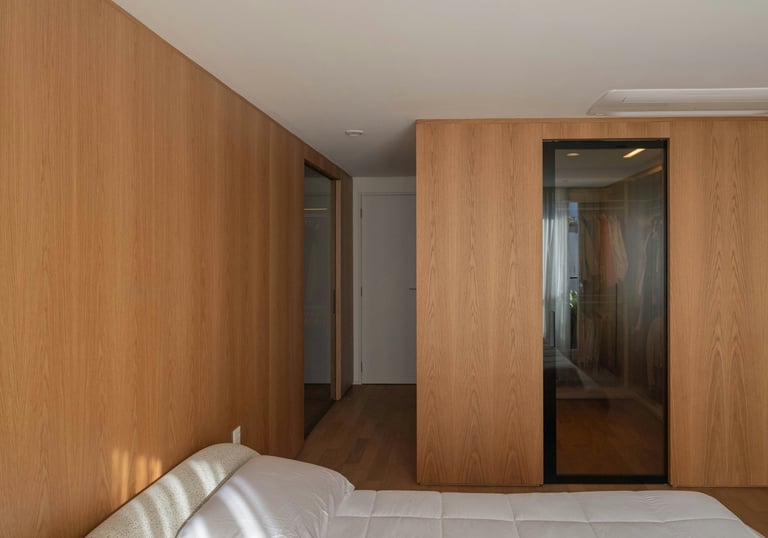 dormitorio calido, revestimiento pared madera clara, puerta vestido de vidrio y puerta de acceso ras