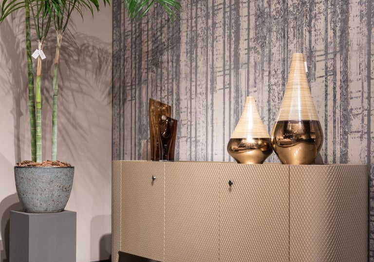 Modern luxury sideboard with decorative gold vases and a tall potted palm plant against textured wallpaper.