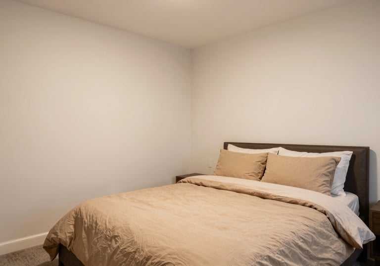 A professional real-estate photograph of a cozy and clean master bedroom. The walls are warm off-white and the bedding is soft tan, creating a welcoming and dependable aesthetic.