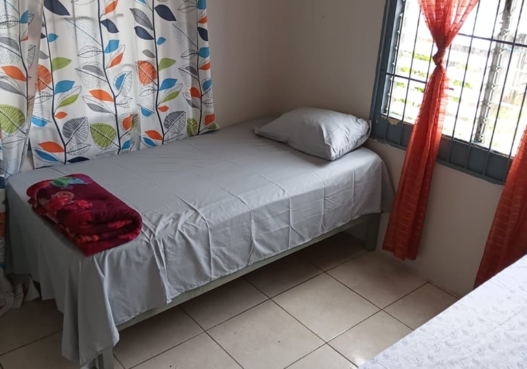 A tidy bedroom featuring a twin bed with grey sheets and colorful leaf-patterned curtains.