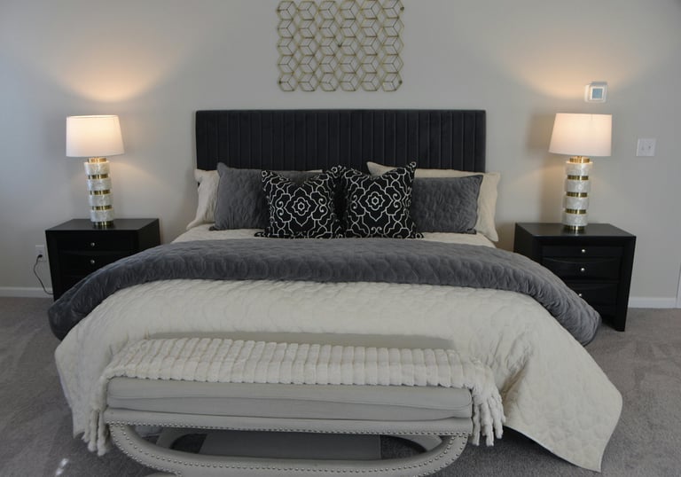 Layered bed with dark upholstered headboard, charcoal and cream bedding, patterned throw pillows, an