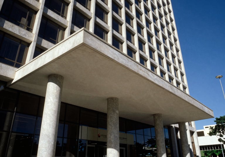 An architectural detail of a modern corporate building entrance in Brazil, focusing on structural strength and professional design, with a deep blue sky backdrop.