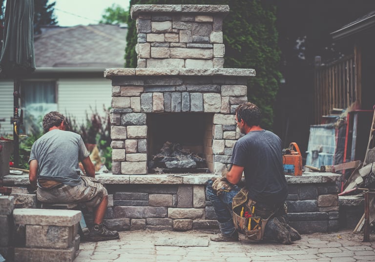 Two professional masons building a custom outdoor stone fireplace on a residential patio.
