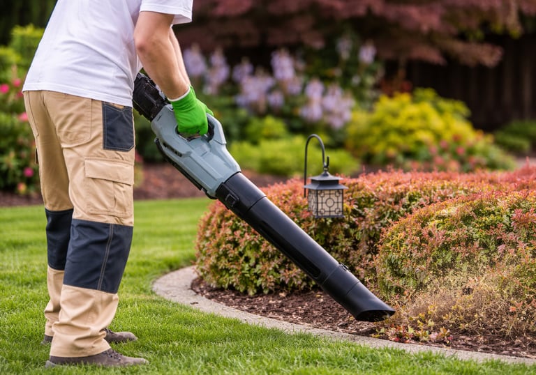 Professional landscaping worker using a leaf blower to clean grass clippings from garden