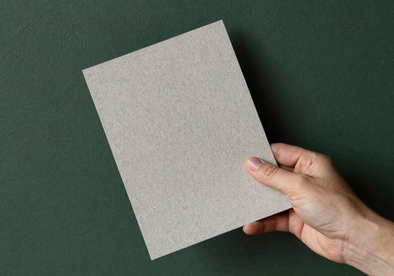 A professional shot of a designer’s hand holding a high-quality textured paper sample against a matte forest green wall.