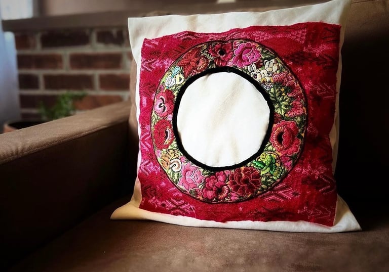 Cojín decorativo bordado a mano de origen guatemalteco con diseño floral sobre un sofá color café.