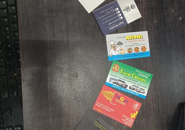 Collection of business cards for local Indian services like tours, hotels, and tile adhesives on a dark desk.