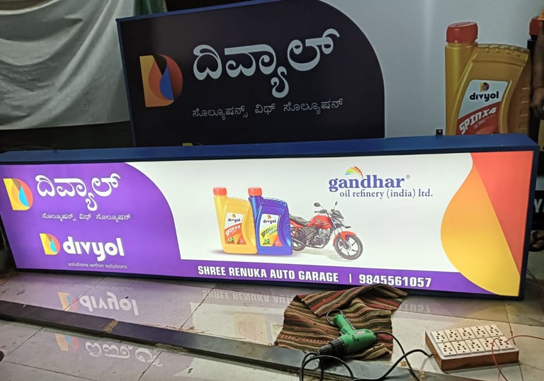 Illuminated shop signboard for Divyol lubricants and Gandhar oil at Shree Renuka Auto Garage.