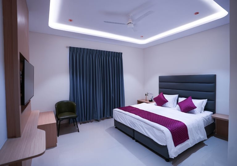 Modern hotel bedroom with purple accents, king bed, and stylish cove ceiling lighting.