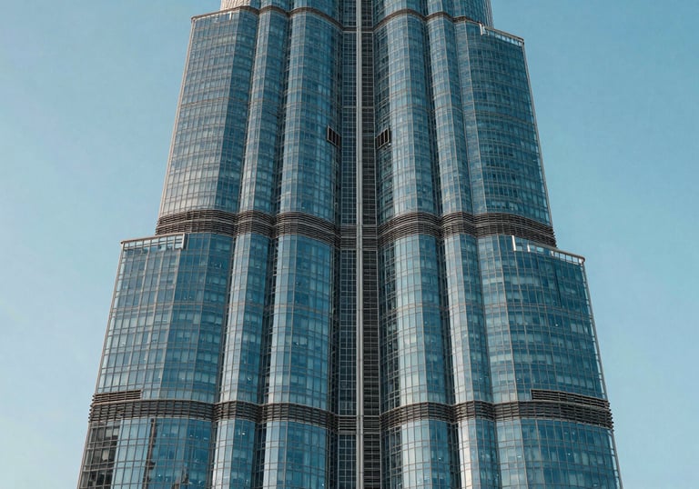 A close-up of a modern glass skyscraper in Dubai reflecting the soft blue and light cyan sky. The architecture is sharp and innovative.