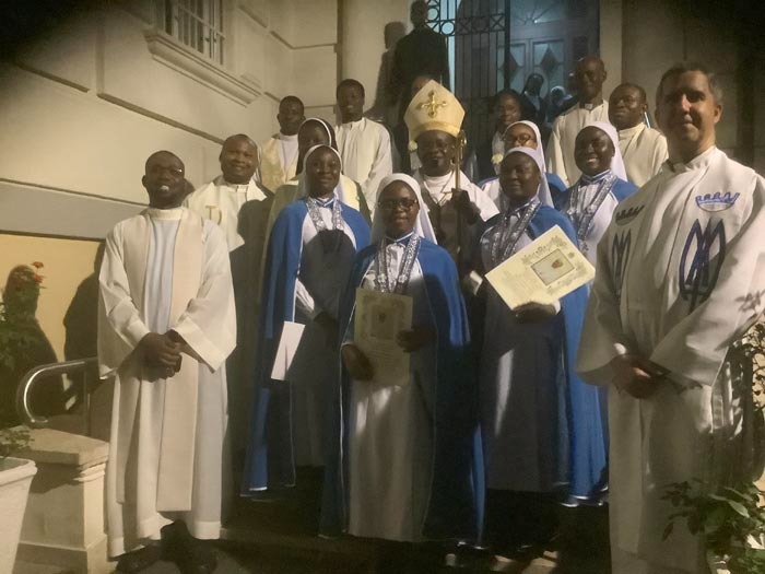 A group of Catholic clergy, including a bishop, priests, and nuns in blue habits, posing for a photo.