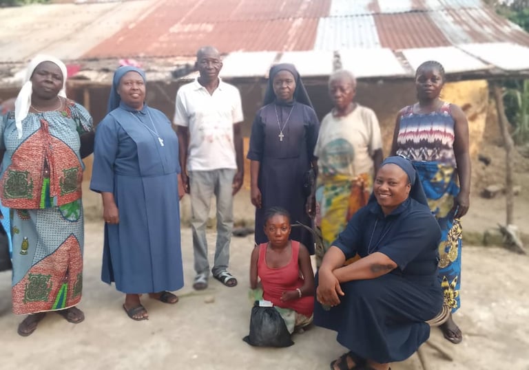 Catholic nuns in habits pose with a local community group in front of a village house for a mission project.