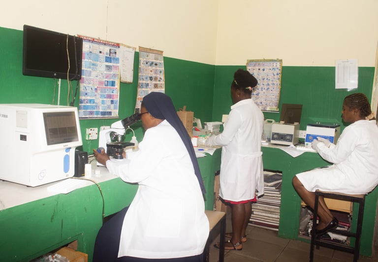 Laboratory technicians in white coats using microscopes and medical equipment in a clinical lab setting.