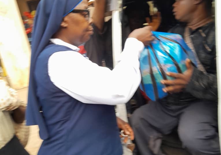 A nun hands a blue relief package to a man in a van during a community charity food distribution.