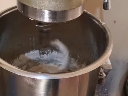 Professional stainless steel stand mixer kneading dough in a large bowl for baking bread.