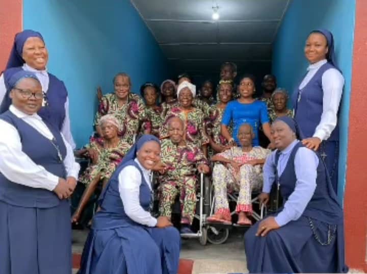 Catholic nuns in blue habits smiling with elderly residents in a community care home setting.