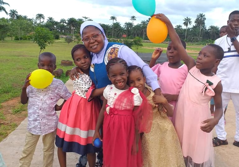 Smiling African children and a nun holding colorful balloons at a community celebration outdoors.