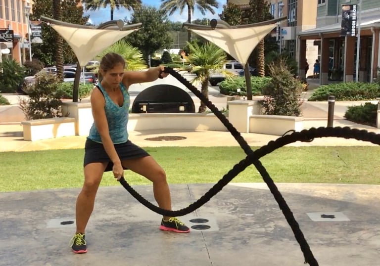A woman performing a high-intensity battle rope workout in an outdoor urban park setting.