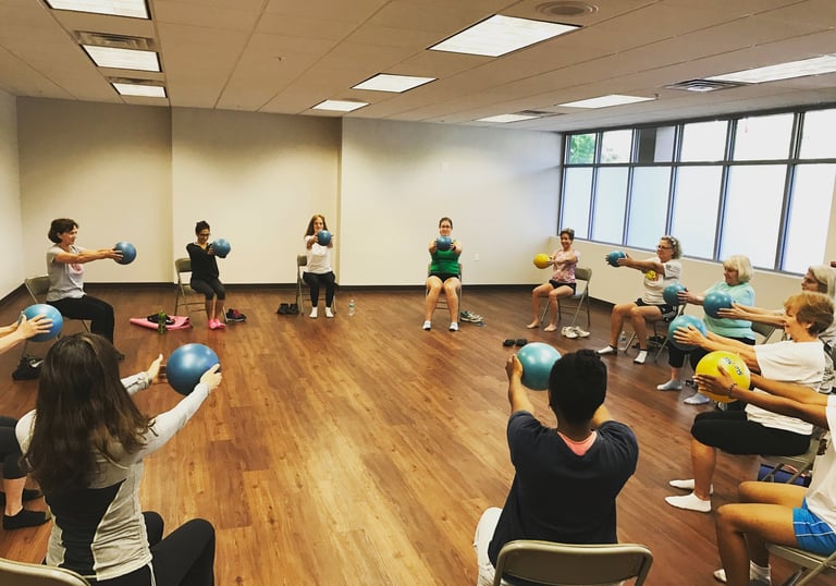 Seniors in a seated exercise class using blue stability balls for a fitness workout in a gym.