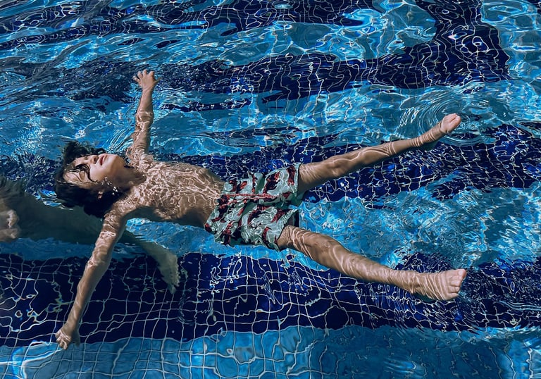 Young boy floating on his back in a blue tiled swimming pool with clear rippling water.