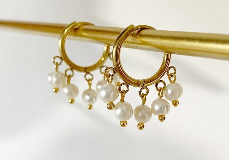 Elegantes aros dorados con dijes de perlas blancas colgantes en una barra de exhibición dorada.