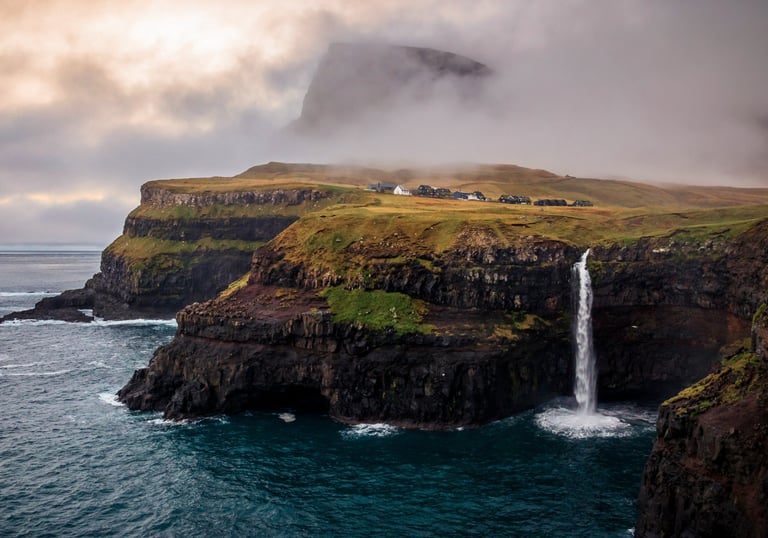 a waterfall falls down a cliff into a body of water. Gásadalur Múlafossur in the Faroe Islands