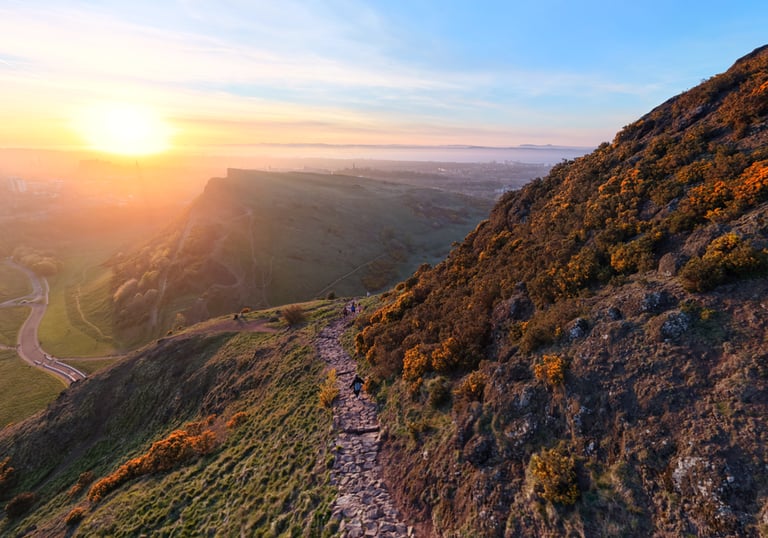A scenic stone hiking trail on Arthur's Seat in Edinburgh at sunset with a view of Salisbury Crags.