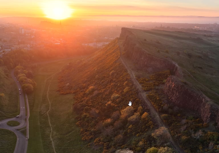 Aerial view of Salisbury Crags in Edinburgh at sunset with the city skyline in the background.