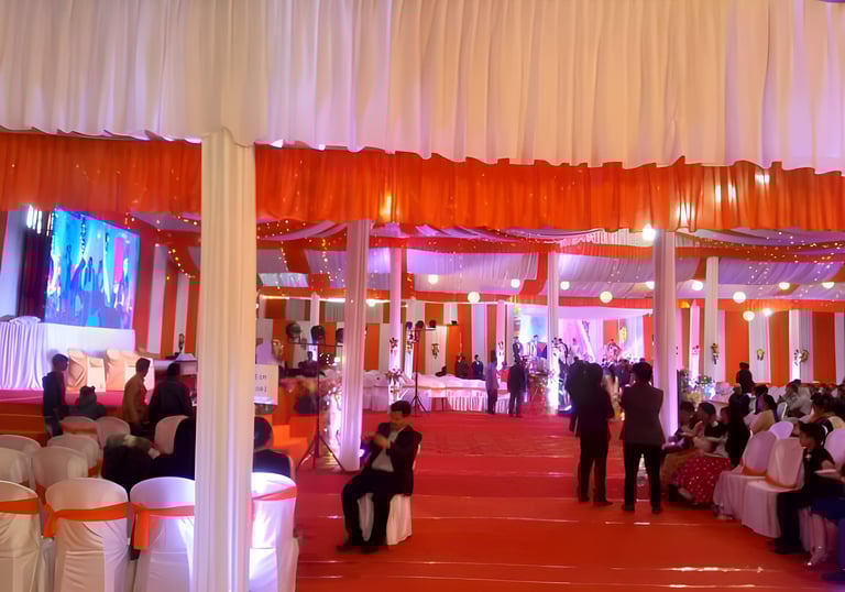 Indoor wedding reception with orange and white decorations, guests seated on white chairs.