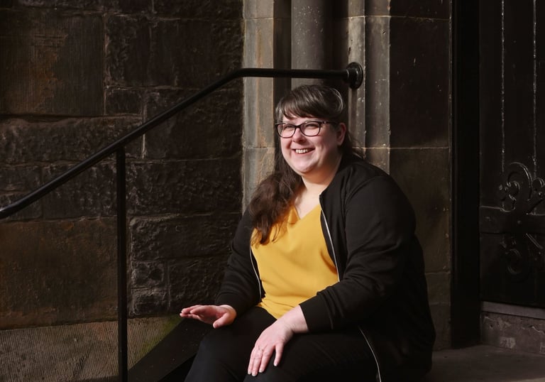 Laura is sitting on stone steps and smiling just away from the camera in direct sunlight