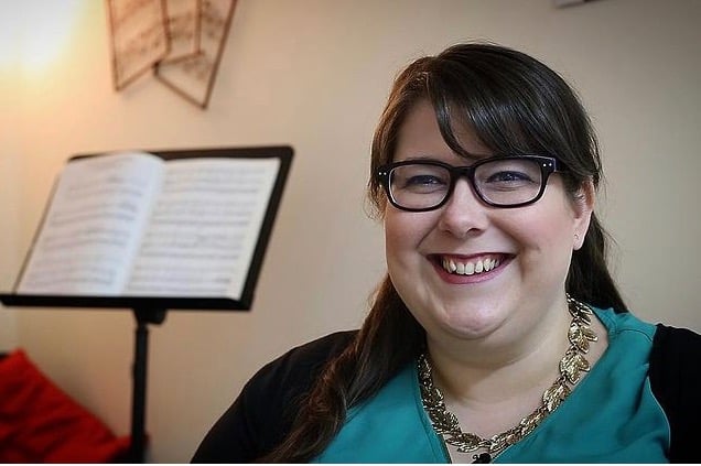 Laura is smiling just off camera and sitting in front of a music stand with music on it