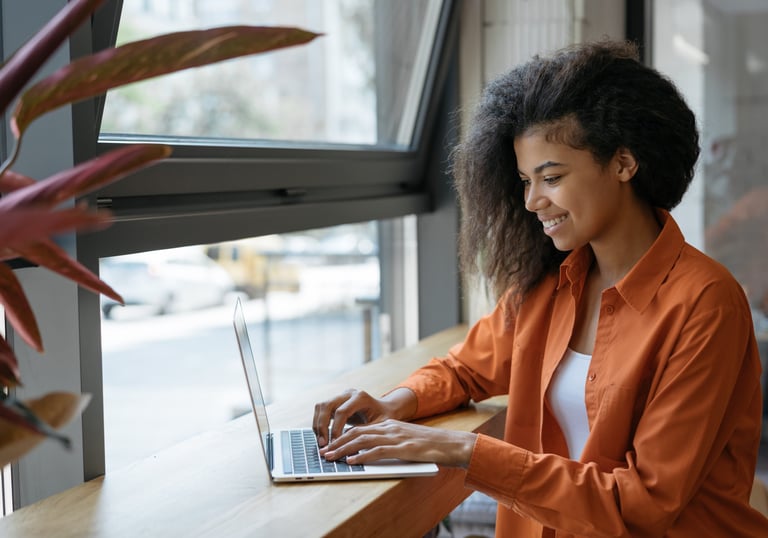 Smiling woman working on a laptop by a window, representing career growth, focus, and momentum