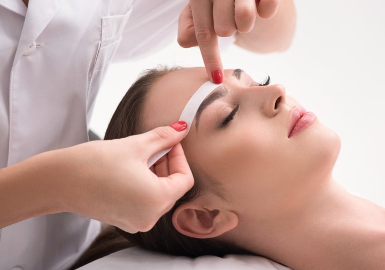 una mujer recibiendo cera facial de una mujer con una camisa blanca en un salón