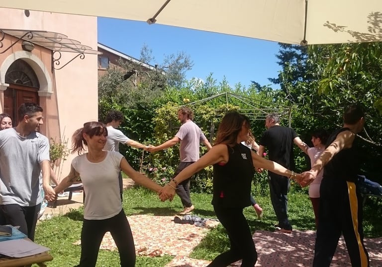 a group of people holding hands and dancing in a garden, classe di bioenergetica