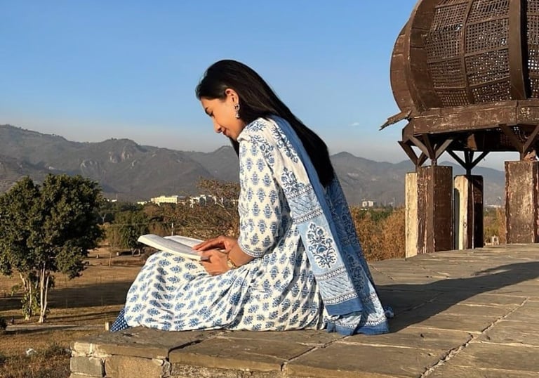 A solo female traveler sits on a bench in Islamabad, absorbed in reading a book. Sunlight filters th