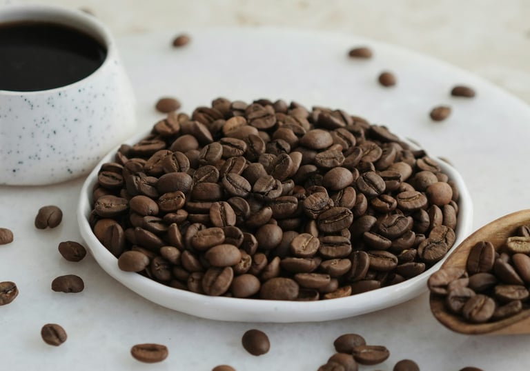 A plate filled with freshly roasted coffee beans with a mug of black coffee in the background