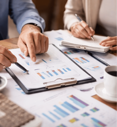 Dos personas revisando documentos y gráficos en una mesa, representando asesoría profesional con seg