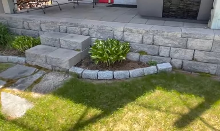 grey brick patio on the rear of a house with steps made of stone with manicured lawn