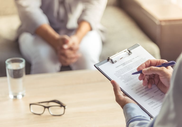 Zwei Personen in einer Psychotherapiesitzun. Der Psychotherapeut macht sich Notizen.