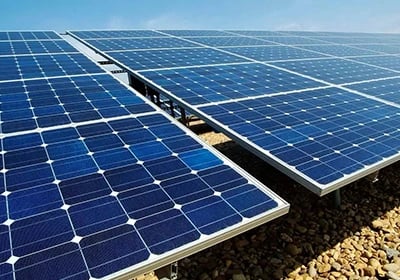 Photovoltaic solar panels installed on a gravel surface under a clear blue sky for renewable energy.