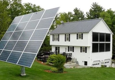 Ground-mounted solar panel array tracking the sun next to a residential home with solar thermal collectors.