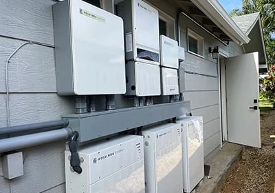 Residential solar energy storage system with Holu Hou Energy battery backup units installed on an exterior wall.