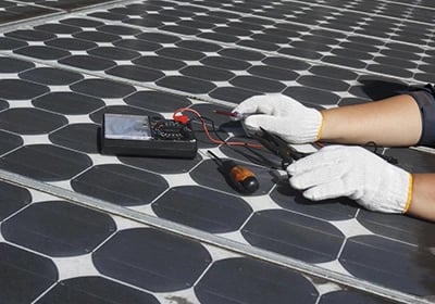 A technician performing solar panel maintenance using a multimeter and tools on a residential roof.