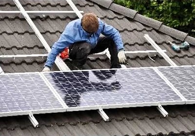Professional technician installing solar panels on a residential tiled roof for renewable energy.