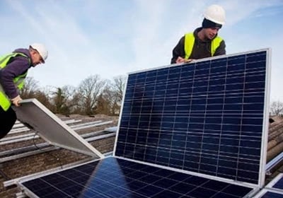Professional solar installers in hard hats and safety vests fitting solar panels on a rooftop.