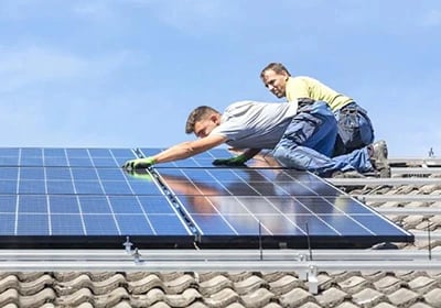 Professional solar panel installation by technicians on a residential tiled roof.