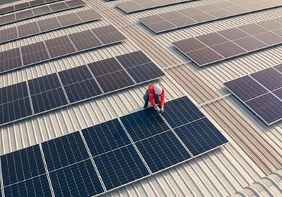 A technician installing solar panels on a commercial metal rooftop for renewable energy.