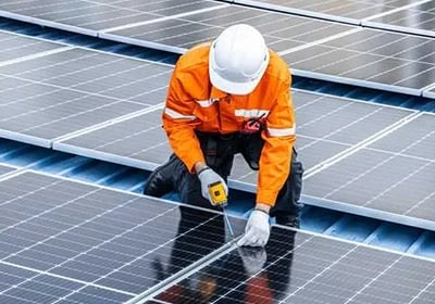 Professional technician in high-visibility gear installing solar panels on a rooftop.