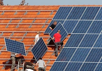 Professional technicians installing blue solar panels on a red tile residential rooftop for renewable energy.
