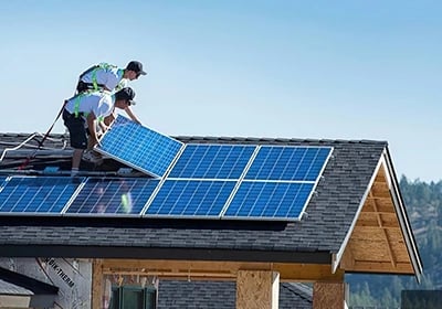 Professional solar installers mounting blue photovoltaic panels on a residential asphalt shingle roof.
